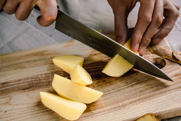 Рука шеф-кухаря ріже свіжу і смачну картоплю для приготування їжі на столі. Здорова їжа
. - Фото, зображення