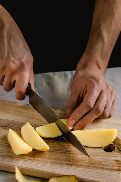 Chef's hand cutting fresh and delicious potatoes for cooking on a table. Healthy food. - Photo, Image