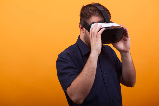 Bearded young man wearing VR headset over yellow background - Foto, imagen