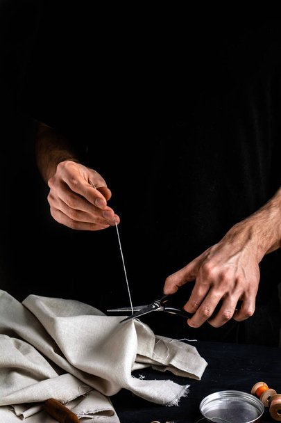 Schneider schneidet einen Faden mit der Schere, Nahaufnahme, schwarzer Hintergrund - Foto, Bild
