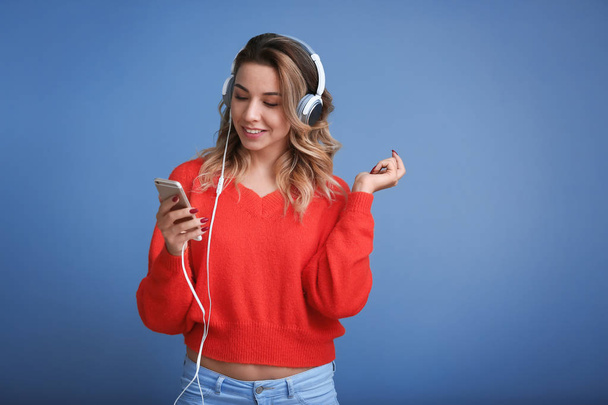 Portret van mooie jonge vrouw luisteren naar muziek op kleur achtergrond - Foto, afbeelding