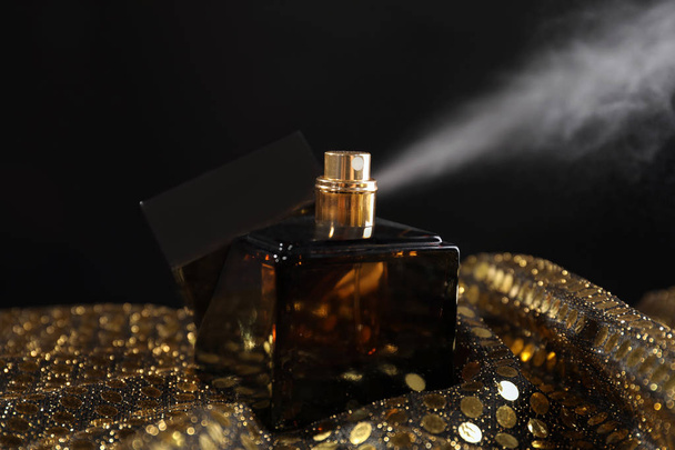 Bottle of perfume on sequin fabric against dark background - Photo, Image