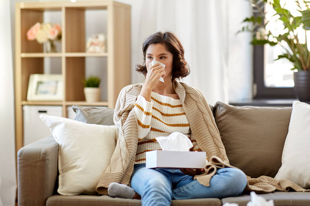 sick woman blowing nose in paper tissue at home - Foto, Bild
