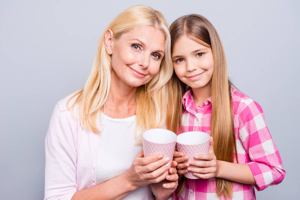 Close up photo funny blond hair she her grandma support little granddaughter hold hot beverage stand close each other relaxing wear casual pink plaid checkered shirt sweater isolated grey background - Foto, Bild
