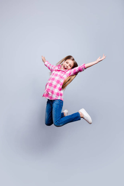 Full length vertical side profile body size photo blond haired she her little cheerleader jump achievement wear casual shoes jeans pink plaid checkered shirt outfit clothes isolated grey background - Fotografie, Obrázek