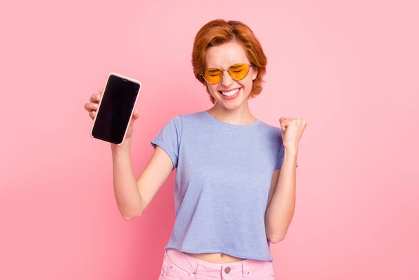Portrait of her she nice cute charming attractive lovely cheerful cheery glad girl wearing casual blue t-shirt yellow glasses holding in hands new cell isolated on pink pastel background - Valokuva, kuva