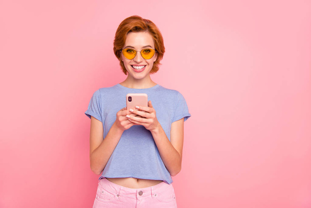 Portrait of her she nice cute charming attractive lovely sweet winsome cheerful cheery girl wearing casual blue t-shirt yellow glasses holding in hands cell isolated on pink pastel background - Φωτογραφία, εικόνα