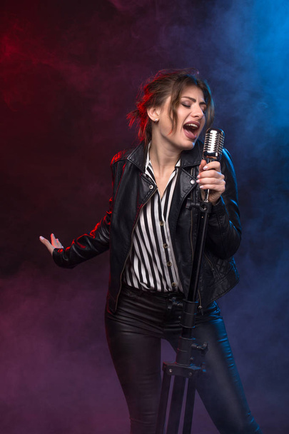 Portret ekspresyjny piosenkarki na sobie skórzaną kurtkę i utrzymanie stylu retro mikrofon. - Zdjęcie, obraz