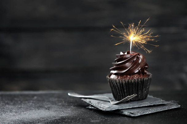 Delicious birthday cupcake with sparkler on dark table - Fotoğraf, Görsel