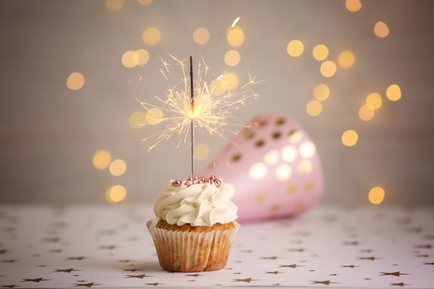 Delicioso cupcake de cumpleaños con bengala ardiente en la mesa
 - Foto, imagen