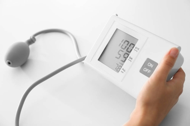 Mujer midiendo presión arterial con esfigmomanómetro sobre mesa blanca
 - Foto, imagen
