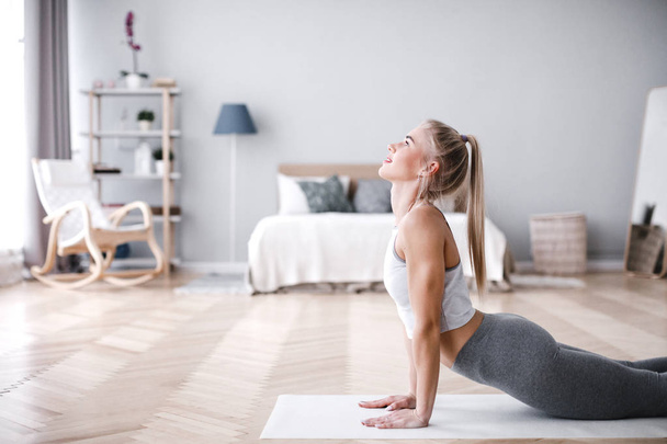 Young sporty woman doing morning exercise in living room on mat. - Fotoğraf, Görsel