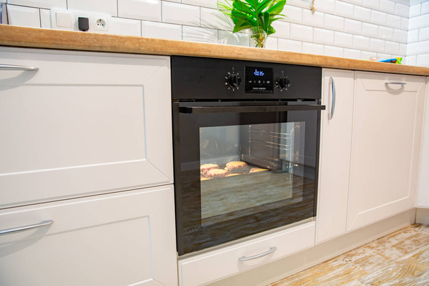 Las chuletas se hornean en el horno en la cocina moderna blanca
 - Foto, Imagen