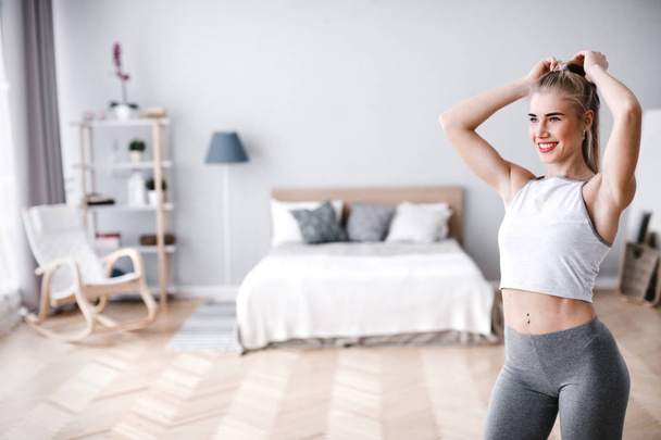 Young sporty woman doing morning exercise standing in living room. - Фото, зображення