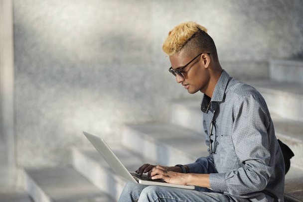 Boční pohled mladého černocha zaneprázdněn prací na notebooku venku - Fotografie, Obrázek