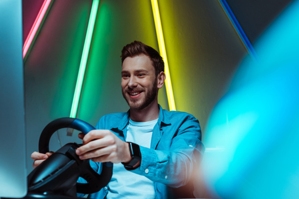 selective focus of handsome and smiling man playing video game with steering wheel - Photo, Image