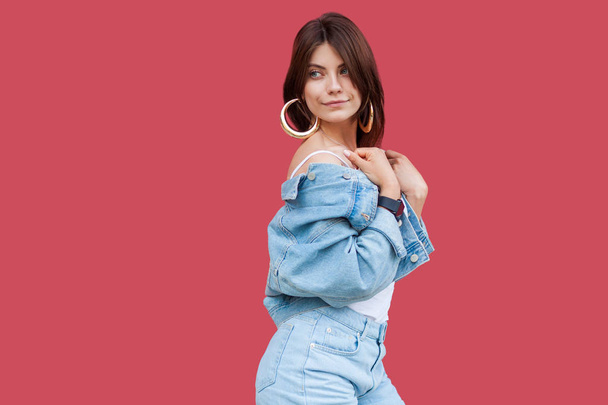 Portrait of fancy beautiful brunette young woman with makeup in denim casual style posing and looking away on red background. - Foto, afbeelding