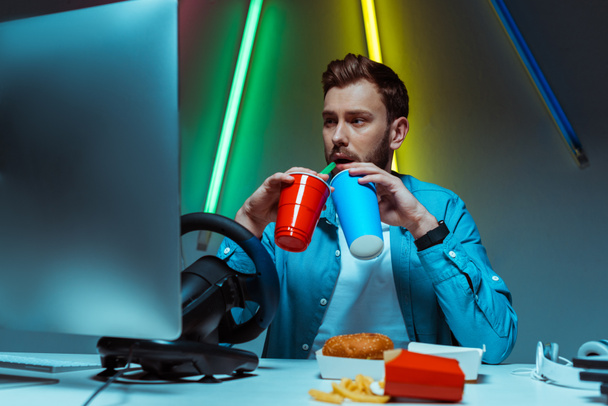 handsome and good-looking man drinking from plastic and paper cups and looking at monitor  - Photo, Image