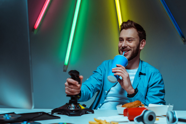 handsome man holding joystick and drinking soda from paper cup  - Foto, immagini