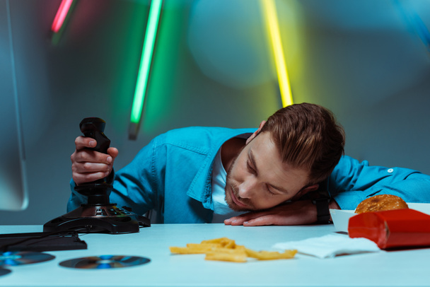 όμορφος νέος ενήλικος άντρας κοιμάται στο τραπέζι και κρατώντας joystick  - Φωτογραφία, εικόνα