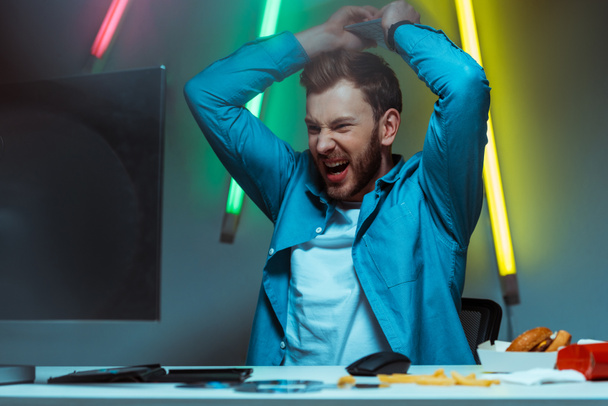 good-looking and angry man holding computer keyboard and screaming  - Photo, Image