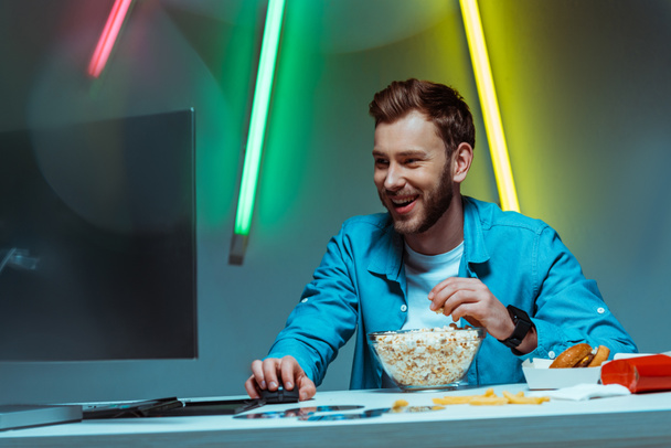 hombre guapo y sonriente sosteniendo el ratón de la computadora y comiendo palomitas de maíz
  - Foto, imagen