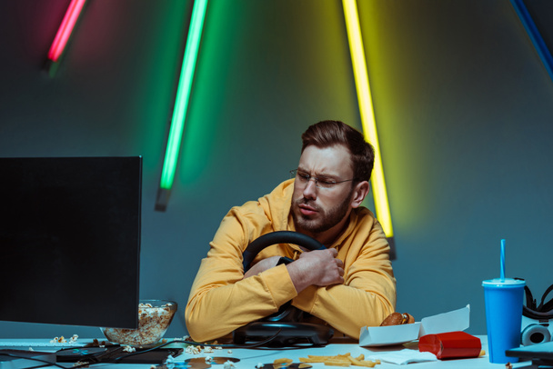 handsome and good-looking man in glasses holding steering wheel and looking at computer monitor  - Фото, зображення
