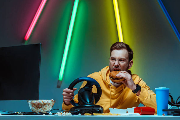 bel homme aux lunettes jouant avec le volant et mangeant un hamburger
  - Photo, image