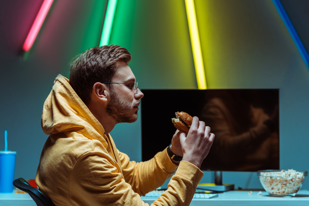 ハンサムで若い大人の男性のサイドビューおいしいハンバーガーを食べて、それを見て  - 写真・画像