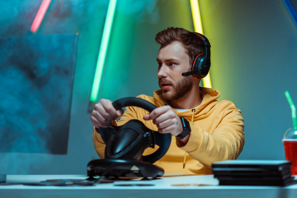 jonge volwassen en knappe man in een koptelefoon spelen van video game met stuurwiel - Foto, afbeelding