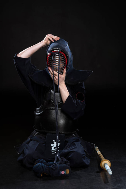 Kendo fighter putting on helmet while sitting on black - Photo, Image
