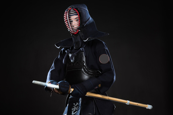 Combatiente Kendo en casco sosteniendo espada de bambú y mirando hacia otro lado en negro
 - Foto, imagen