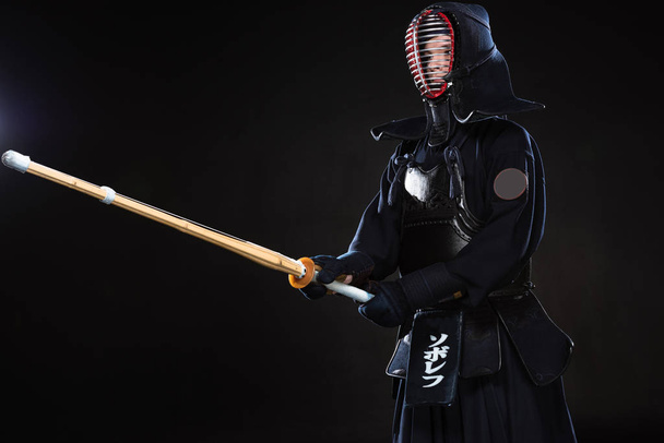 Combatiente Kendo en casco tradicional sosteniendo espada de bambú sobre negro
 - Foto, imagen