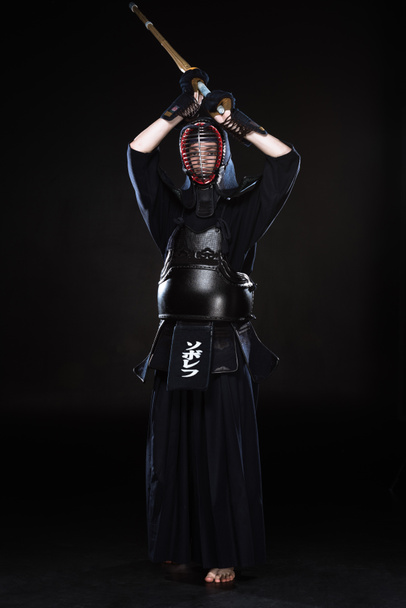Full length view of kendo fighter in armor practicing with bamboo sword on black - Zdjęcie, obraz