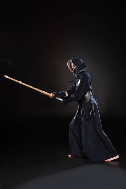 Вид збоку боєць Кендо в обладунках, що практикують з бамбуковим мечем на чорному
 - Фото, зображення