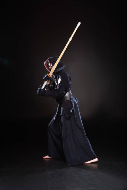 Vue pleine longueur du combattant kendo en armure pratiquant avec épée de bambou sur noir
 - Photo, image