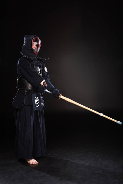 Vista completa del combattente kendo in armatura che si esercita con la spada di bambù sul nero
 - Foto, immagini