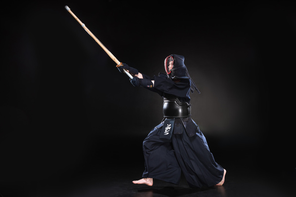 Full length view of kendo fighter in armor practicing with bamboo sword on black - Photo, Image