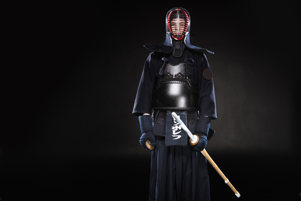 Боец Кендо в доспехах держит бамбуковый меч на черном
 - Фото, изображение