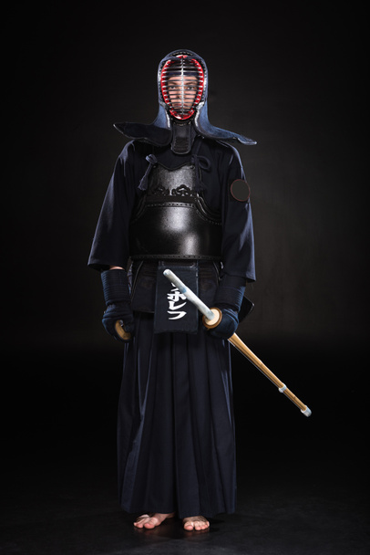 Vista completa de kendo fighter en armadura sosteniendo espada de bambú sobre negro
 - Foto, Imagen