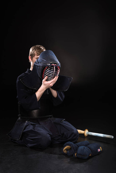 Young man in kendo armor putting on helmet on black - Photo, Image