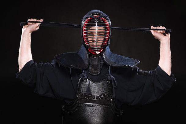 Front view of kendo fighter in armor tying helmet on black - Photo, Image