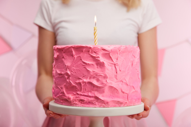 primer plano de la mujer sosteniendo pie de la torta con dulce rosado pastel de cumpleaños y vela ardiente
  - Foto, Imagen