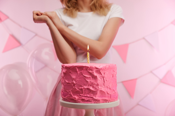 selective focus of cake stand with tasty pink birthday cake and burning candle near woman - Foto, afbeelding
