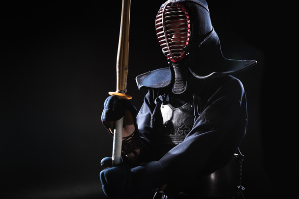Kendo vechter in helm houdt bamboe zwaard op zwart - Foto, afbeelding