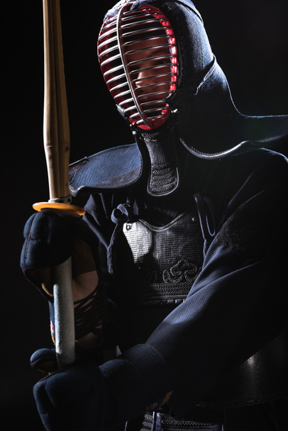 Kendo fighter in helmet holding bamboo sword isolated on black - Photo, Image
