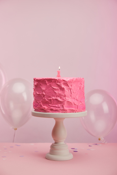 burning number one candle on pink and tasty birthday cake on cake stand near air balloons on pink  - Photo, Image