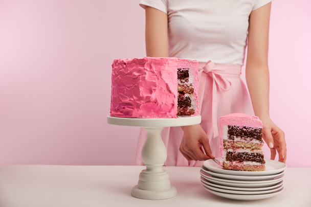 cropped view of woman standing near piece of sweet pink birthday cake in white saucer on pink - Foto, Bild