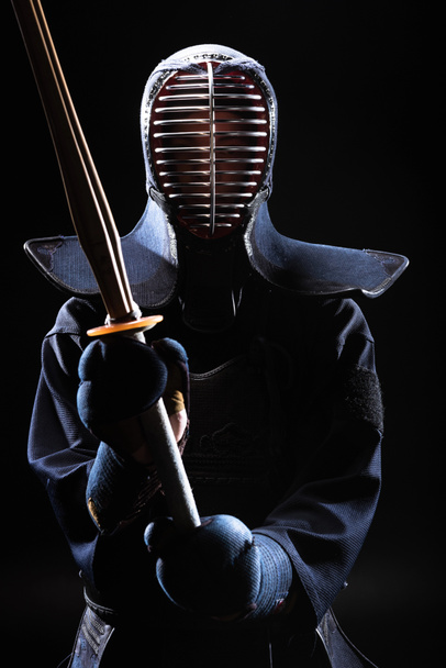 Kendo vechter in helm houdt bamboe zwaard op zwart - Foto, afbeelding