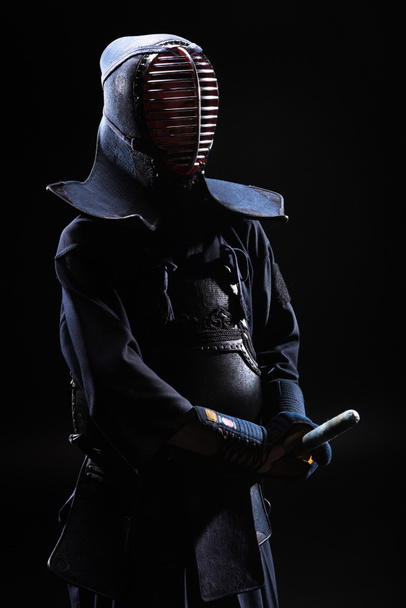 Combatiente Kendo en casco sosteniendo espada de bambú sobre negro
 - Foto, imagen